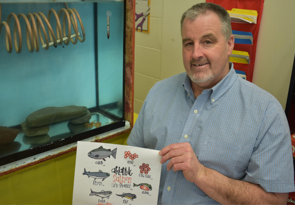 David Sullivan, a Roncalli Elementary grade four teacher, explains the life cycle of Atlantic salmon life stages. In the background, the salmon eggs are hatching. 