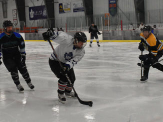 a player skating into the corner with the puck as three opponents chase him down to get the puck at the Paradise Double Ice Complex