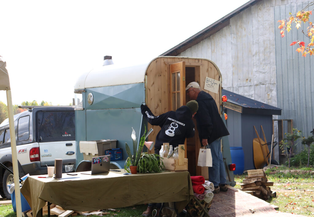 Evan Brown, carpenter and artist, shows customer the sauna he built from an old horse trailer.
