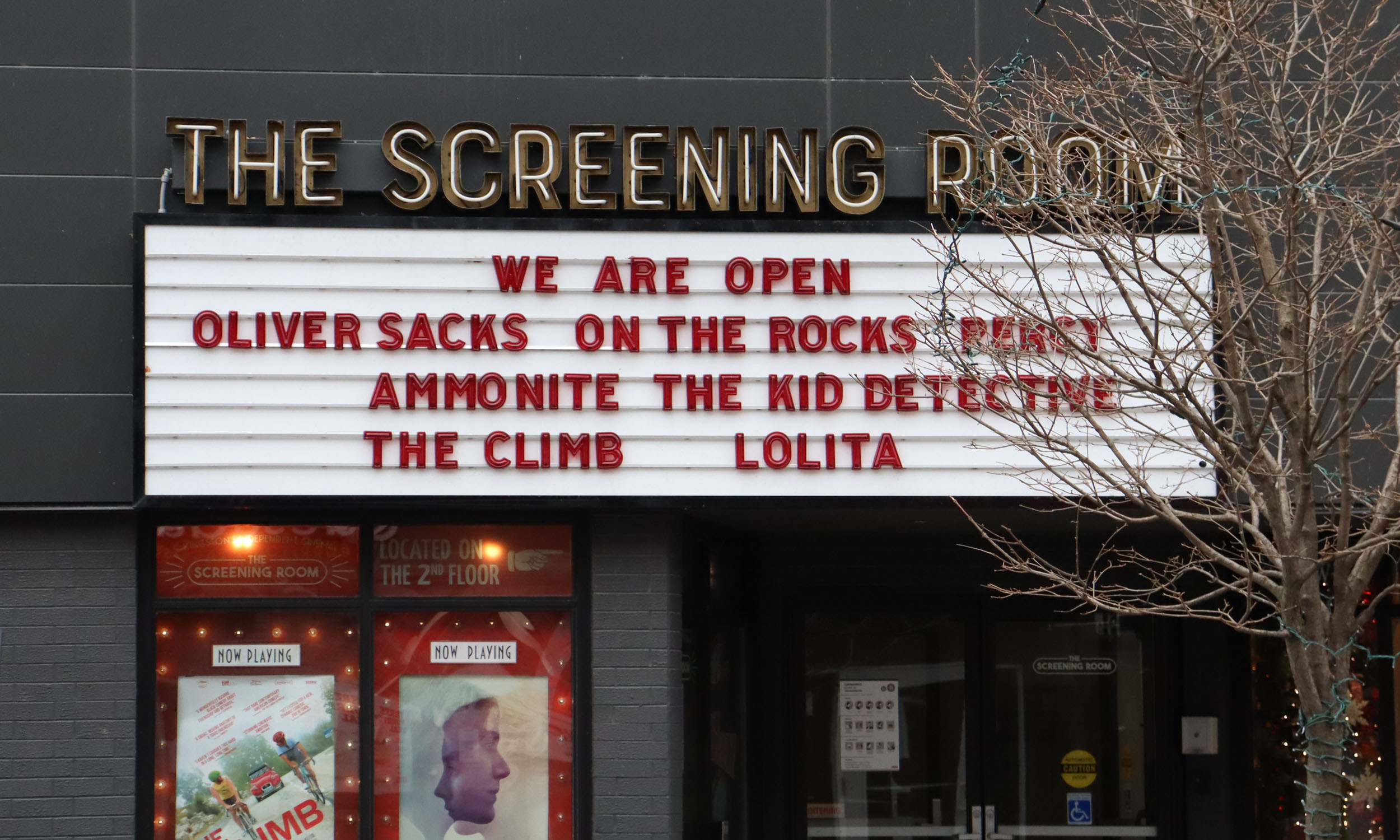 Image of outdoor sign for the screening room. It reads "We are open", with movie titles following.
