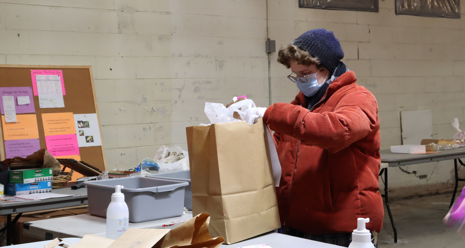 Photo of person working at the farmer's market pick up location. Individual is filling paper bag with food