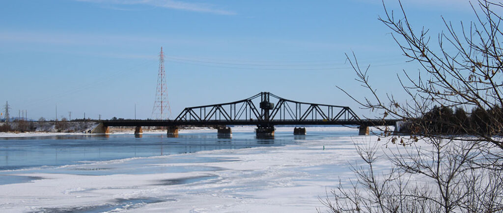 one lane metal bridge spans narrow channel on a bright winter day