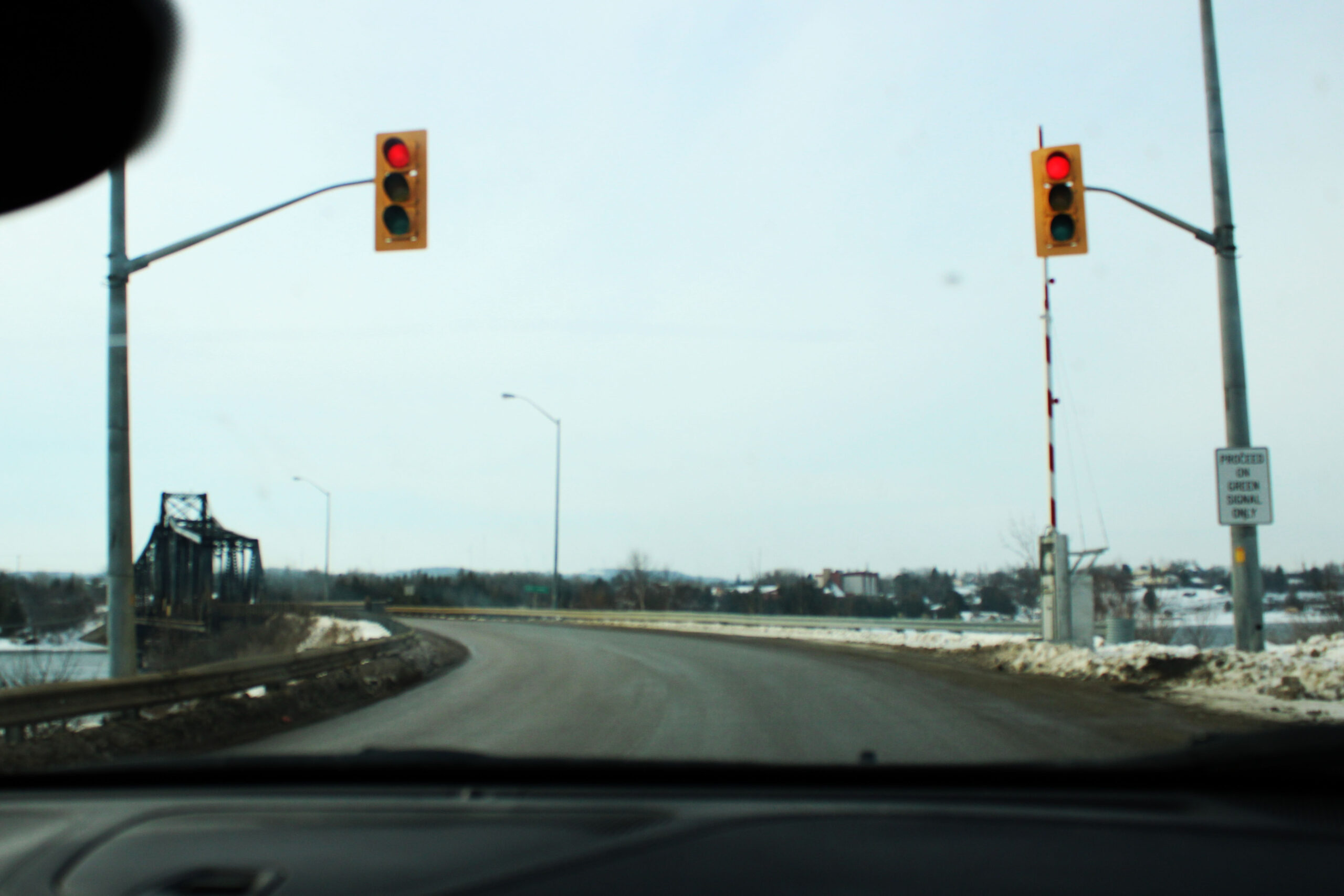 view from dashboard of car of two stop lights in the foreground and a metal bridge in the background