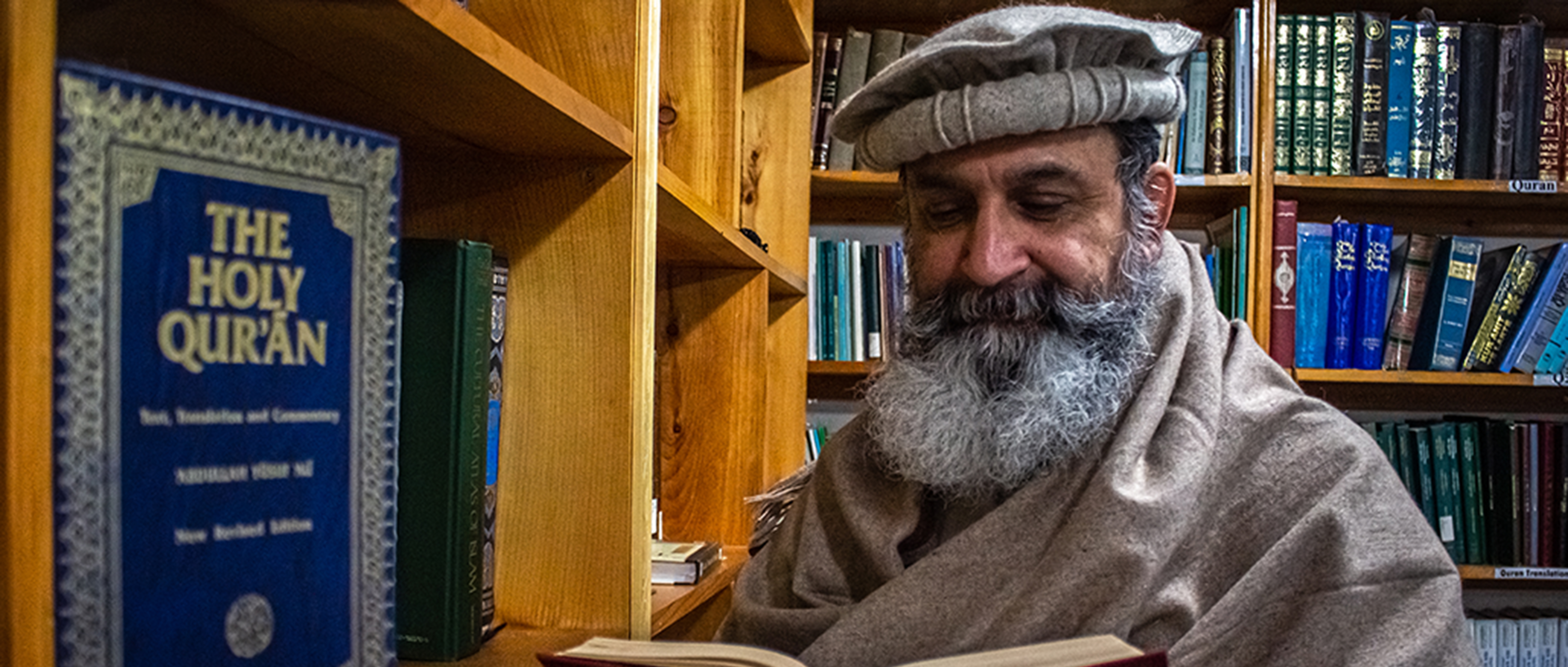 A bearded imam reads a book in the library of a mosque in St. John's, Newfoundland. A blue-covered Koran is visible on a bookshelf. Muslims in St. John's recently commemorated the sixth anniversary of an attack on a mosque in Quebec City.