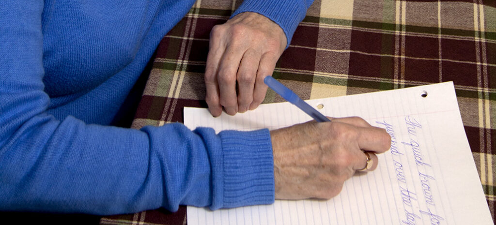 Winnie Cowan holds her paper steady with one hand as she writes in cursive with the other.