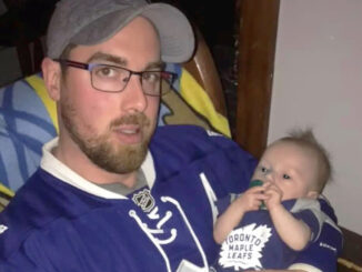 man with beard and glasses wearing a Toronto maple leaf's jersey holds a baby around four months old also wearing the same jersey.