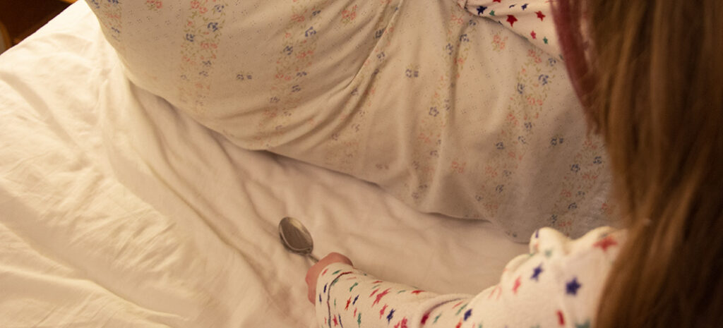 A young girl wearing her pajamas inside out puts a spoon under her pillow.