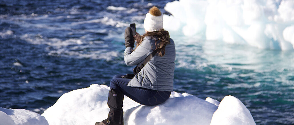 A woman sits on ice taking photos of icebergs