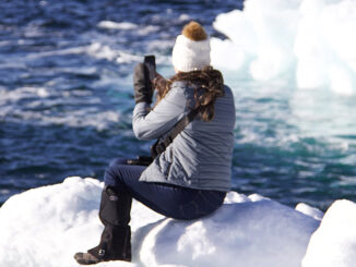 A woman sits on ice taking photos of icebergs