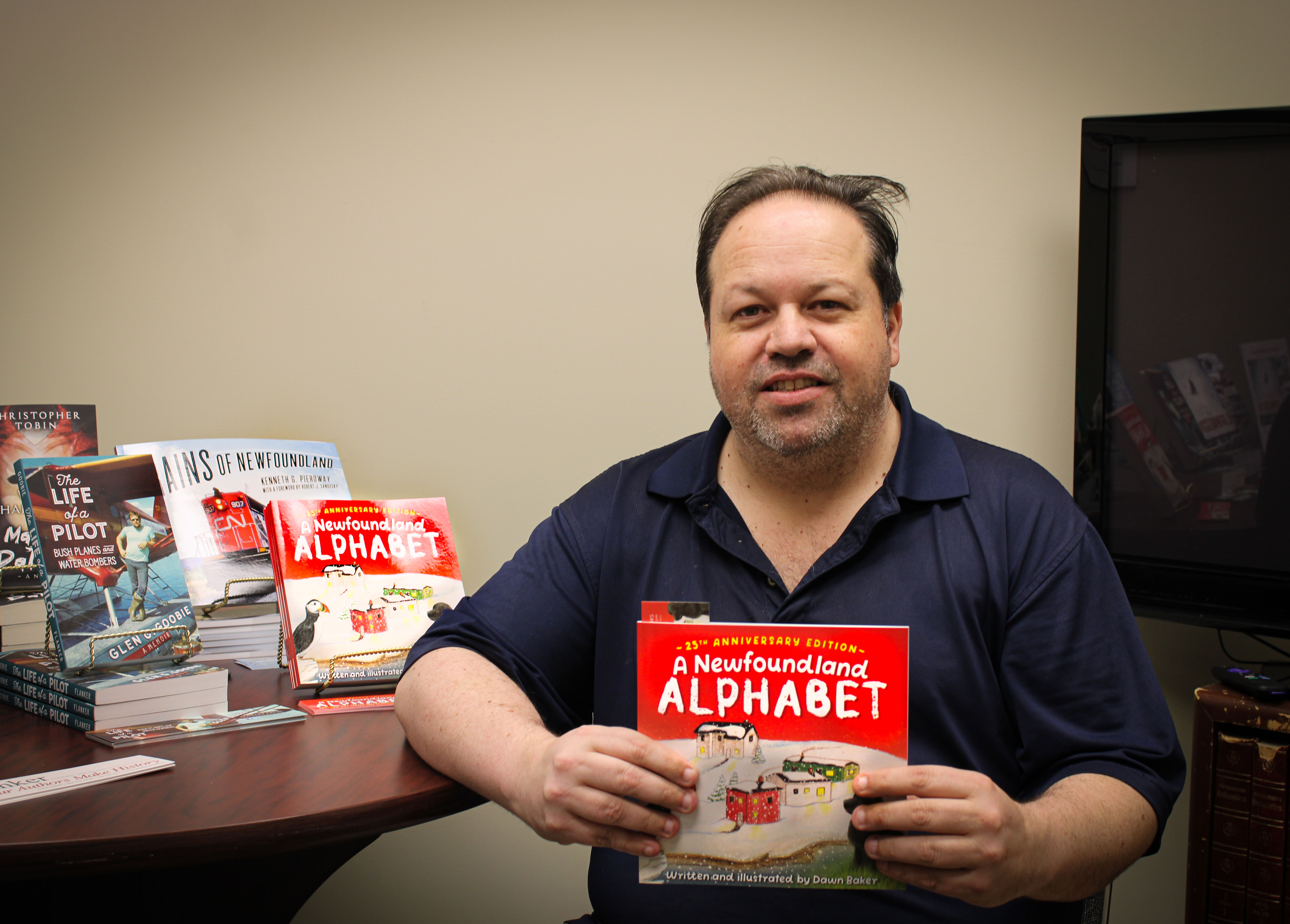 Jerry Cranford, the Flanker Press Ltd publisher holds Dawn Baker's new children's book, A Newfoundland Alphabet. It has a bright red cover with vivid illustrations.