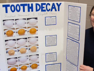 Rachael Hammond stands holding a poster board filled with text and photos of her project titled "tooth decay"
