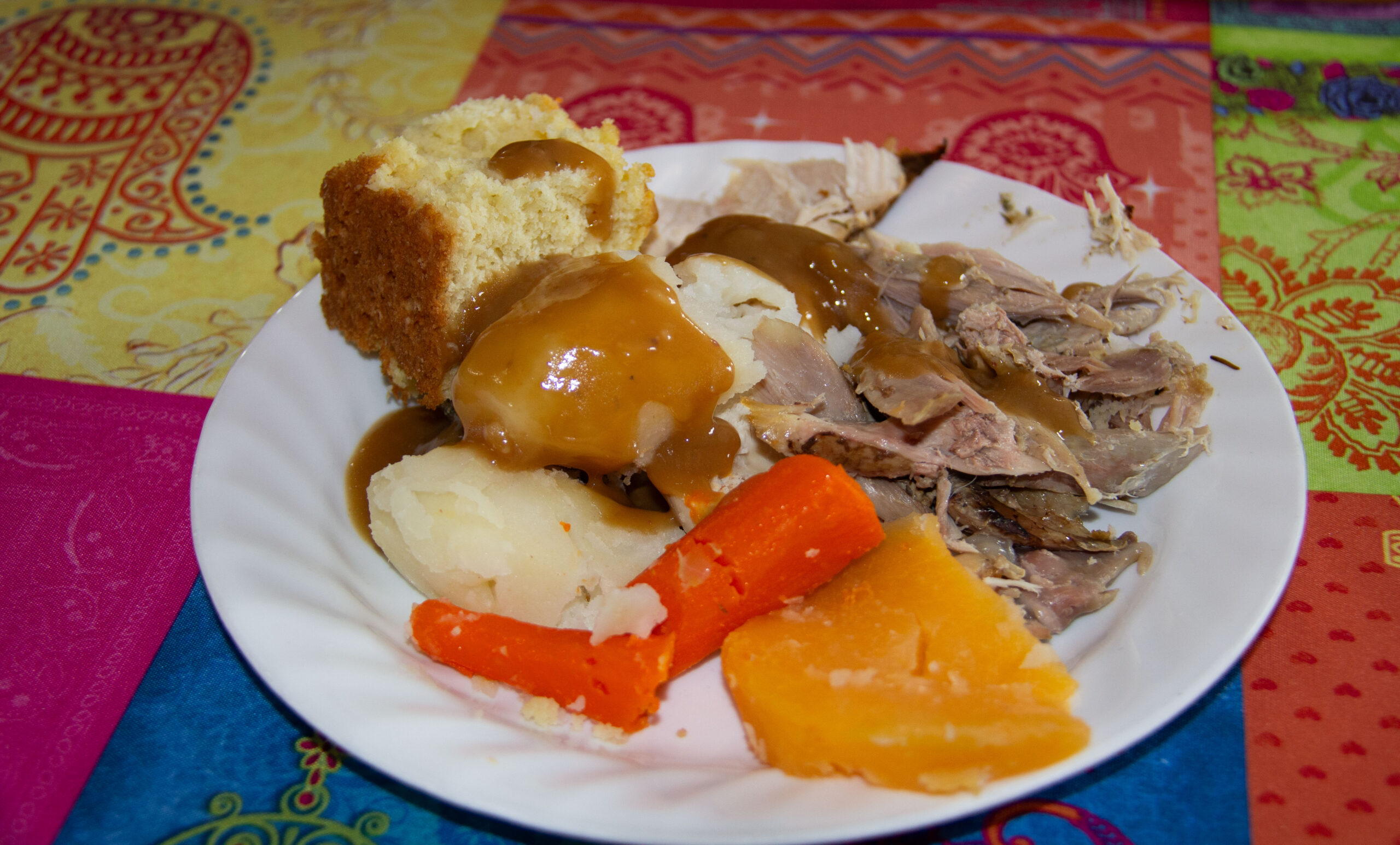 A plate filled with food for Jiggs' Dinner. Veggies, stuffing, turkey, and bread pupping, coated in gravy.