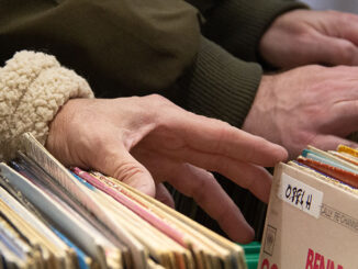 A close-up of a man's hand sorting through a box of records.