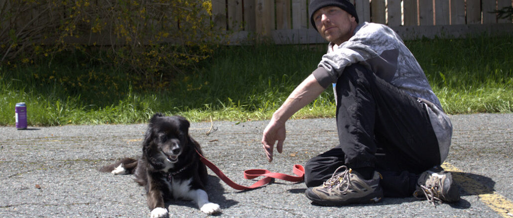Gregory McCain and his dog Maggie sit on a parking lot in the sun. McCain was one of the residents of the "tent city" homeless encampment in St. John's.