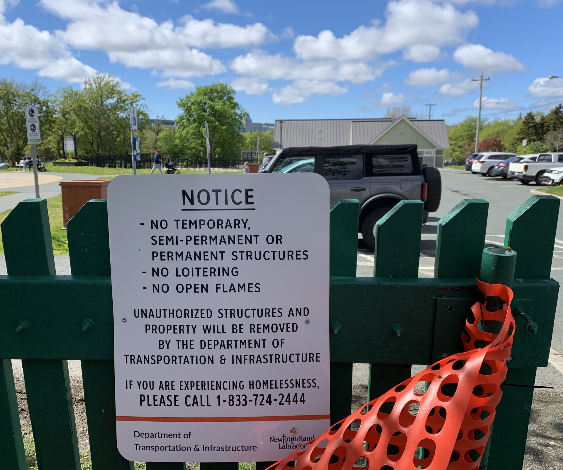 A sign on a fence between the Colonial Building and Bannerman Park reads "No temporary, semi-permanent or permanent structures, no loitering, no open flames. Unauthorized structures and property will be removed by the Department of Transportation and Infrastructure. If you are experiencing homelessness, please call 1-833-724-2444.