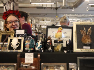 Image shows curious Collections owner, Krista Elliott posed by her stand at the market
