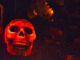 A Lawn is covered in Halloween decorations. Including a graveyard with a gray coloured tombstone and a glowing red skull next to it.