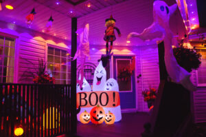 A house is covered in Halloween decorations. The home is lit up in orange and purple lights with inflatable ghost decorations.