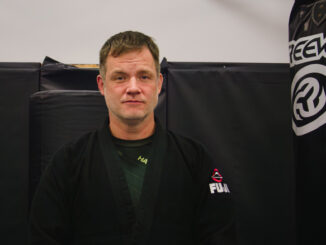 A man wearing a black martial arts gee in a martial arts gym.
