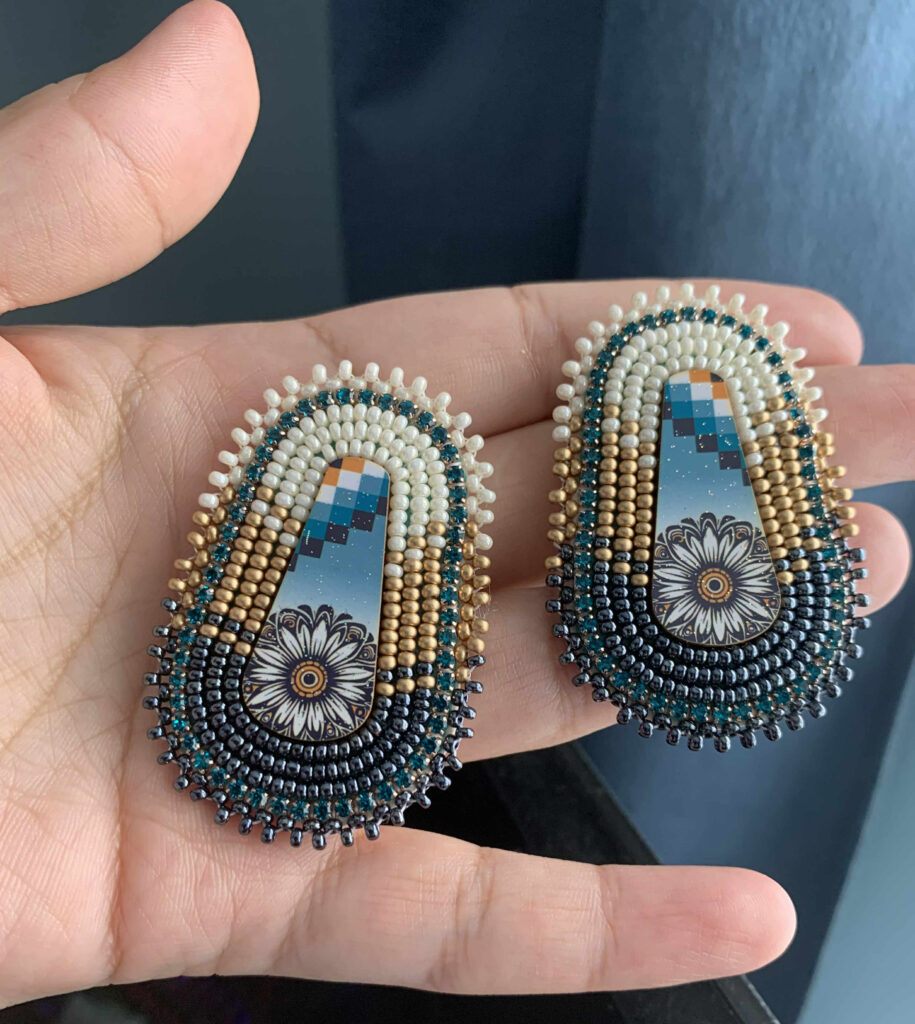 A hand holds a pair of beautifully beaded earrings.