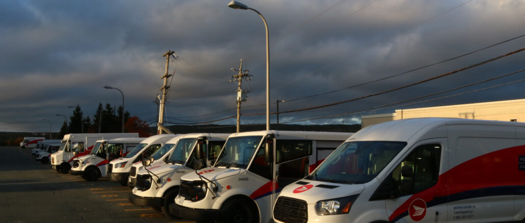 a line of canada post trucks park at sunset.