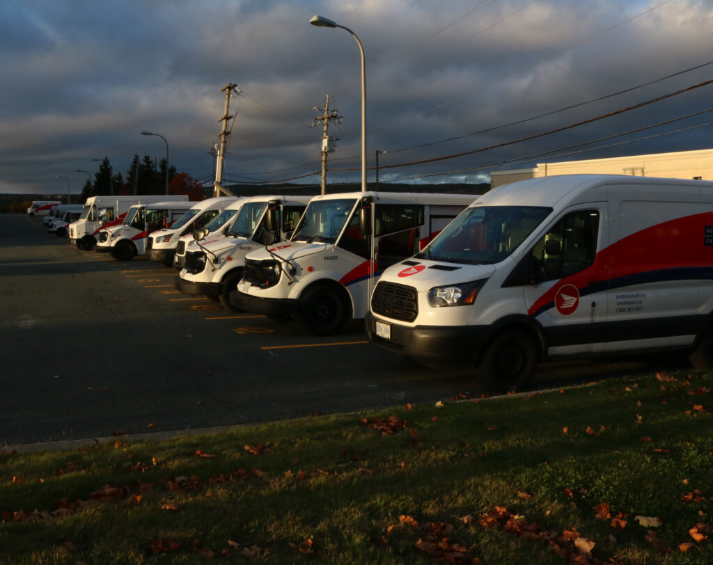A line of Canada Post trucks are lined up at sunset.