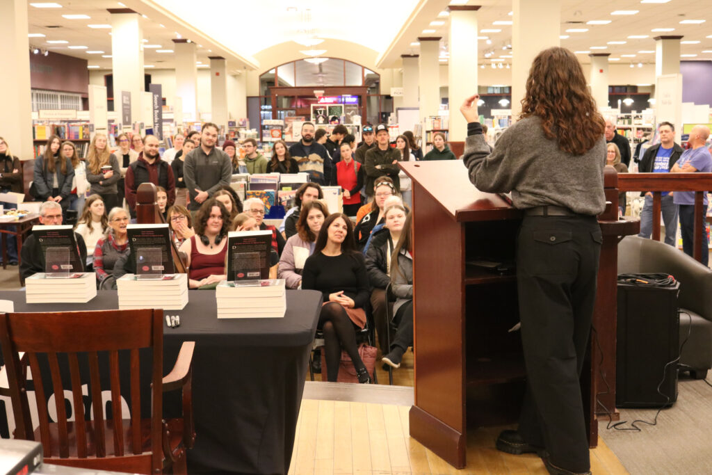 Mackenzie Nolan stands in front of a room full of people at her book launch. 