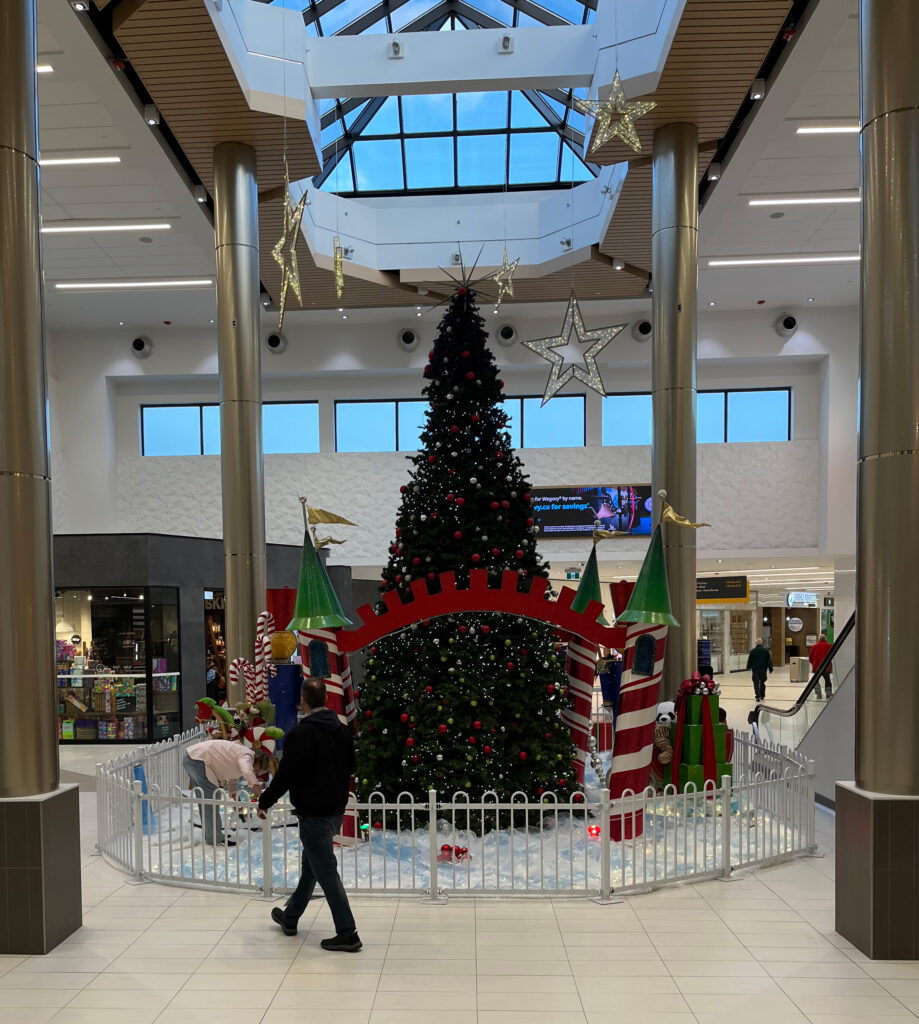 A man walks infront of a woman decorating the christmas tree at the Avalon Mall.