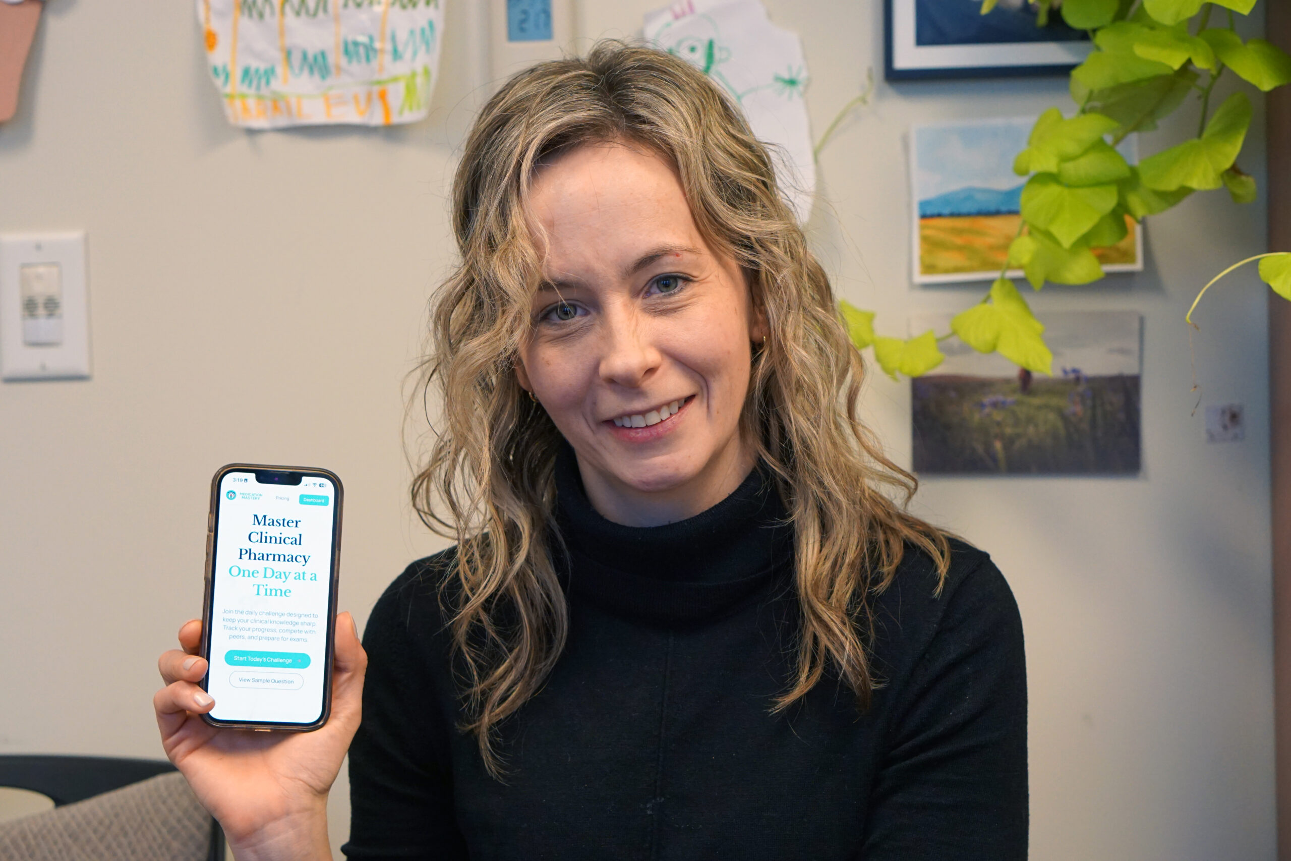 Dr. Catherine Balsom poses for a photo with her phone displaying the homescreen of her app developed with AI.