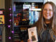 Return of the vhs tape. A woman stands holding 2 VHS tapes in front of a shelf filled with many more.