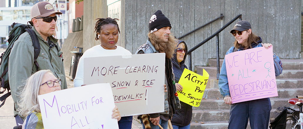 A group of protesters hold signs demanding better snow clearing outside St. John's city hall on Tuesday.